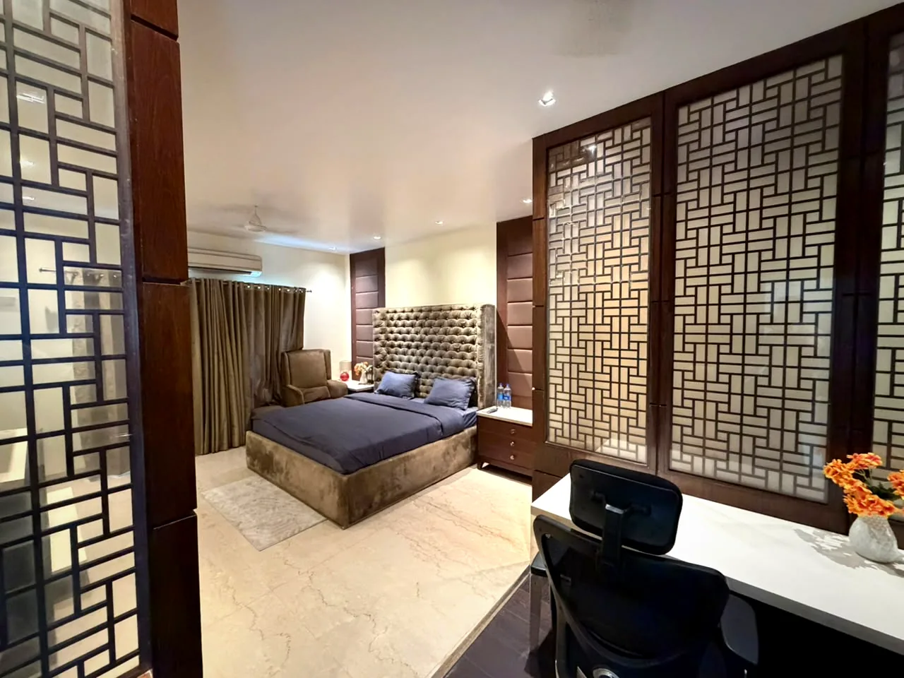 View through wooden lattice screens into a bedroom with study desk at Nivasa Villas